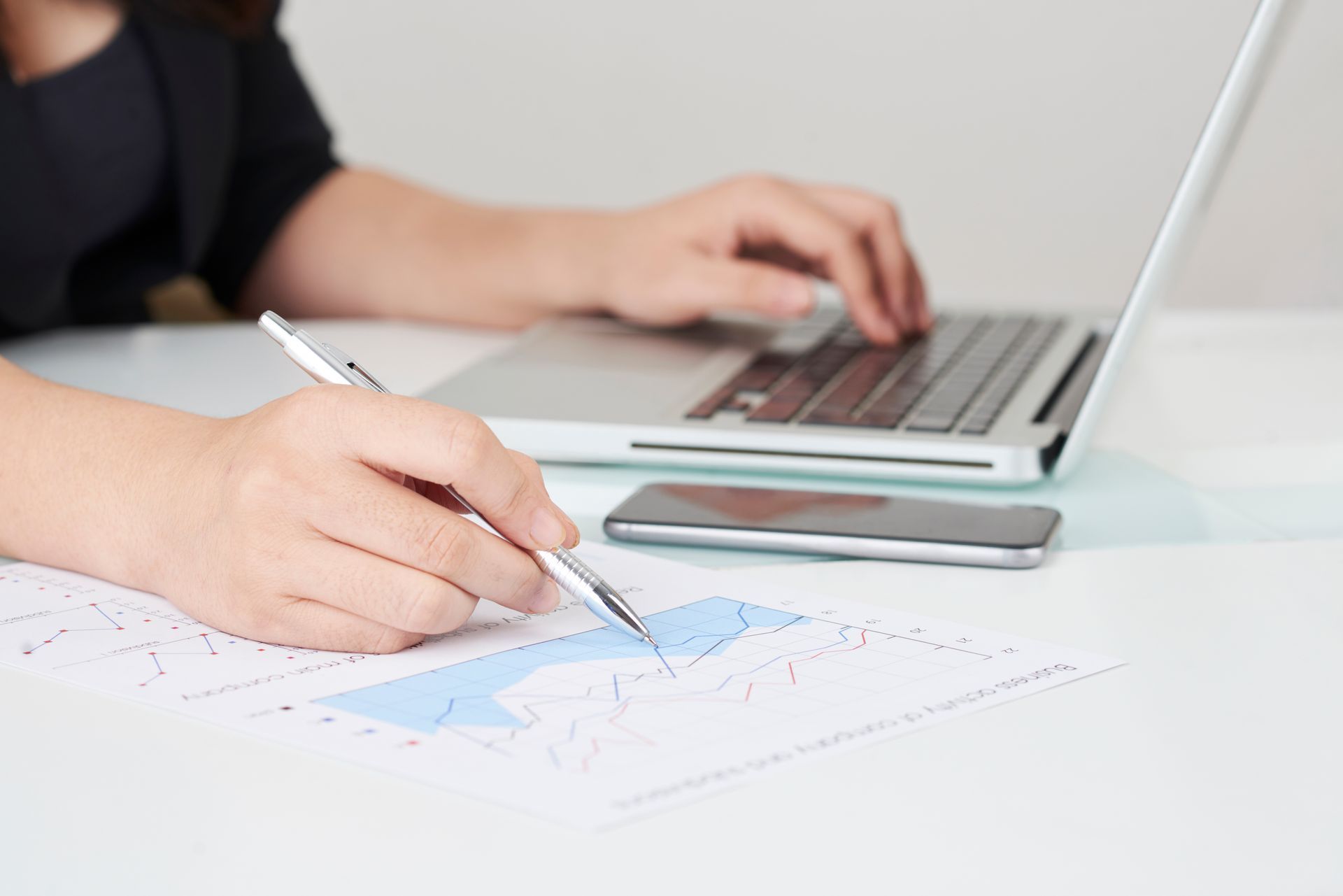 Hand sketching chart data beside a laptop on a white desk