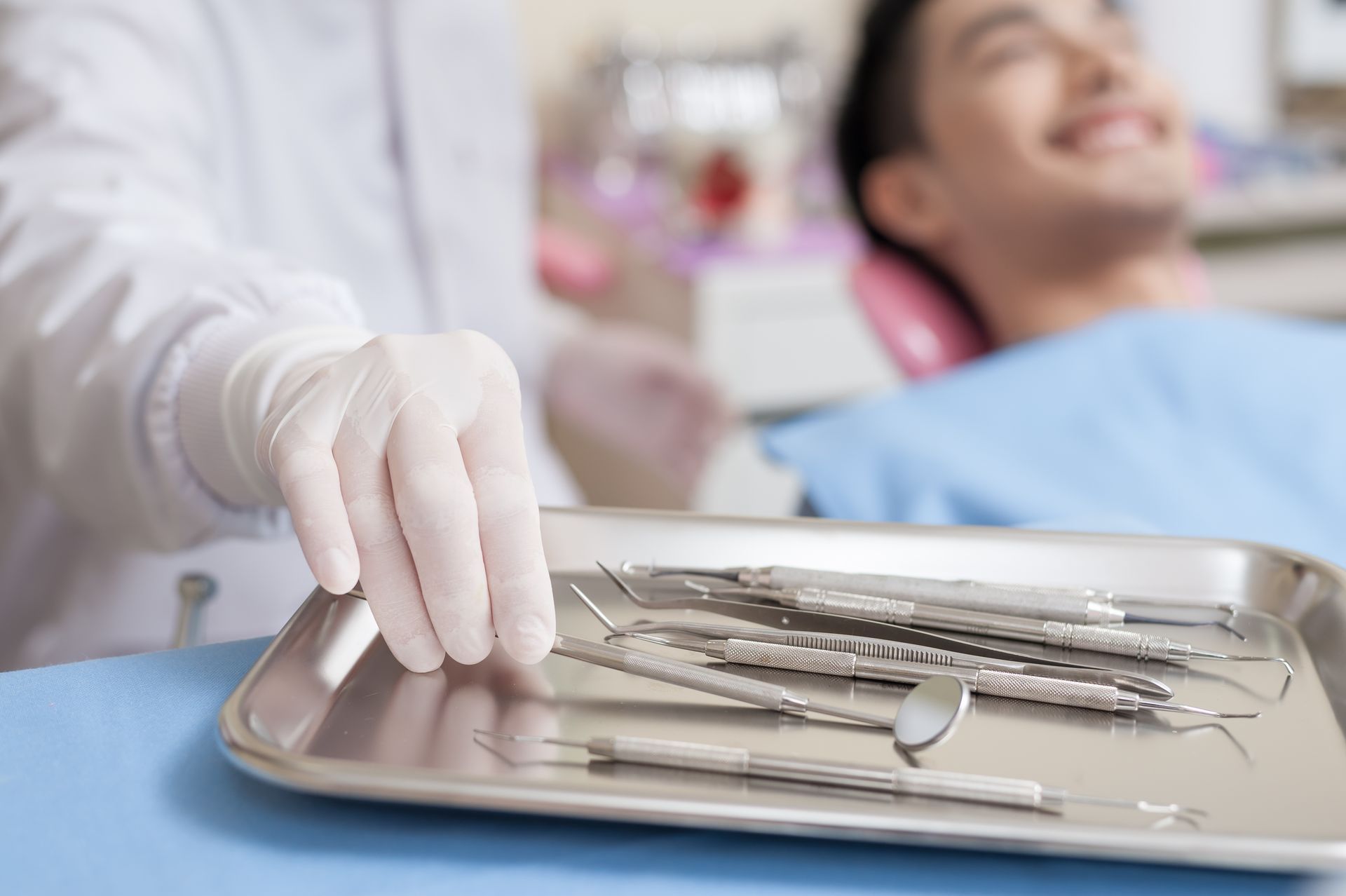 Dentist reaching for dental instruments on a tray during a patient visit. Dentist reaching for dental instruments on a tray during a patient visit.