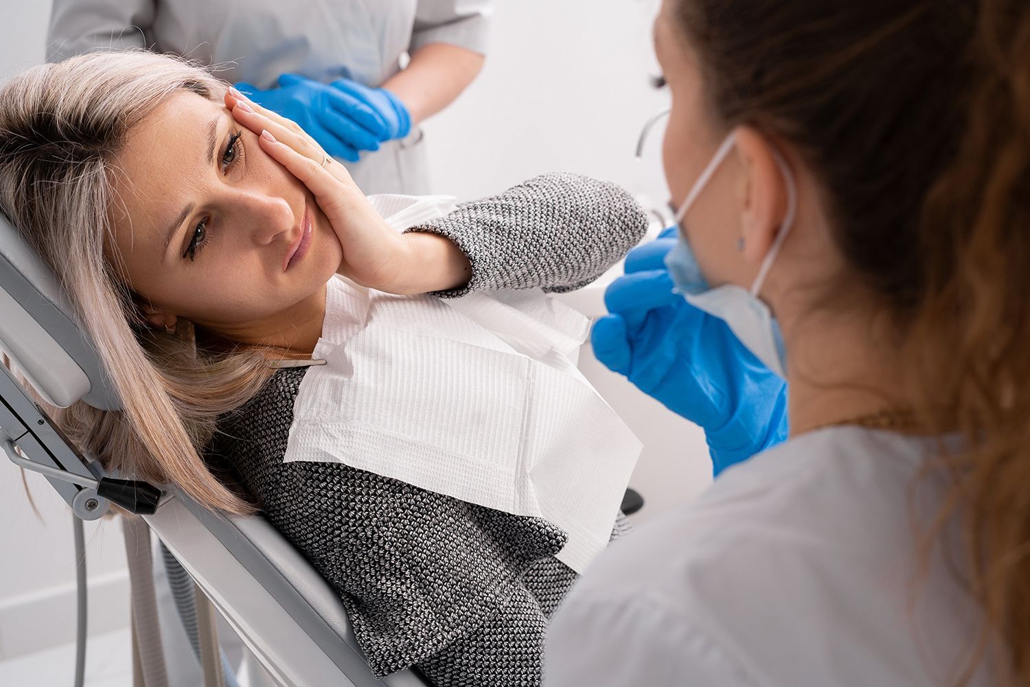A dentist examining a patient in a reclined chair with an assistant nearby A dentist examining a patient in a reclined chair with an assistant nearby
