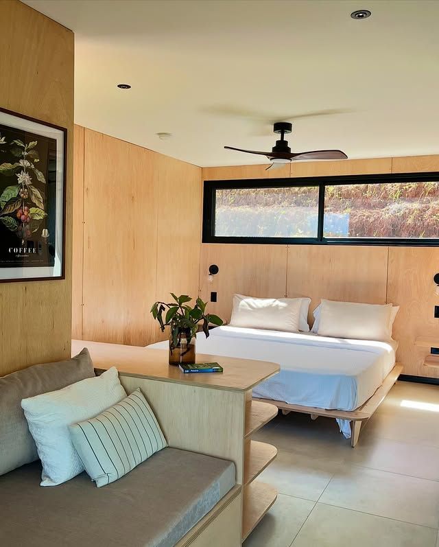Modern living room with wooden walls, gray sofa, white daybed, and a vase of colorful flowers on a round table