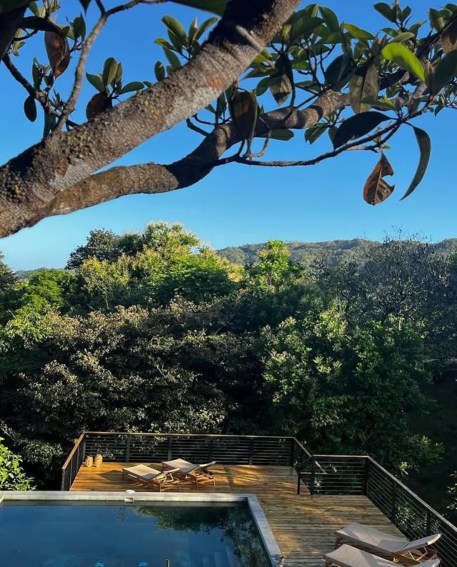 Poolside deck with railing, lush green trees, and a distant mountain under a blue sky.