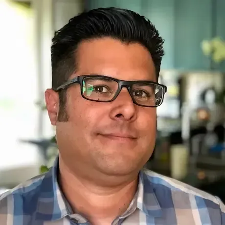 Portrait of a person wearing black glasses and a blue plaid shirt, indoors with a blurred background