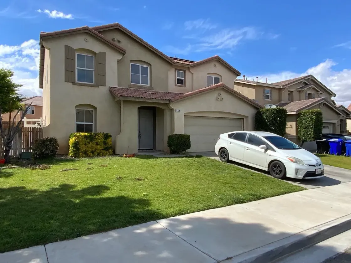 Single-story house with gray tiled roof, fenced front yard, and trimmed hedge on a quiet street