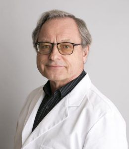 Portrait of a man in glasses and a white coat against a plain background