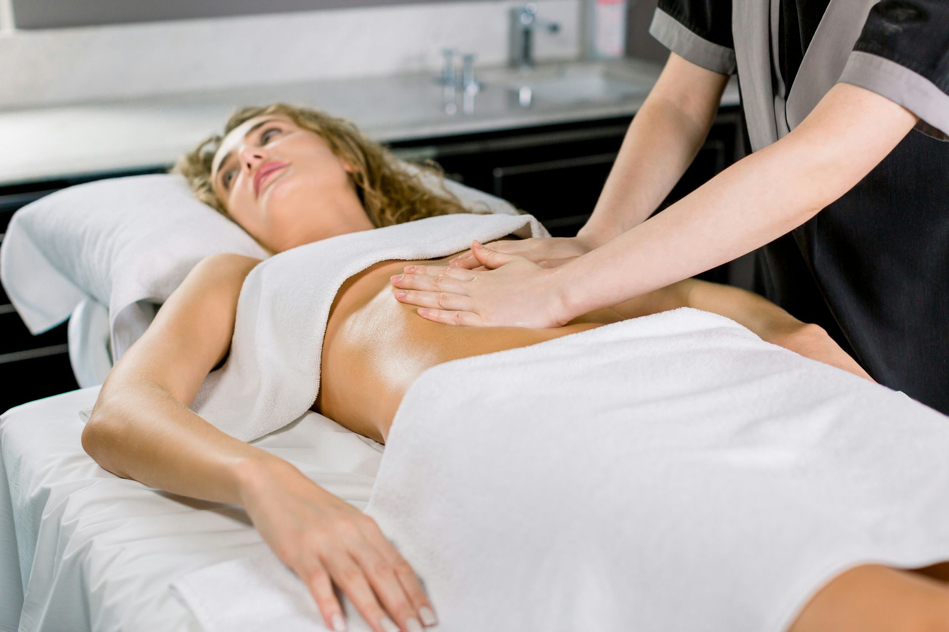 Massage therapist applying back massage to a woman lying on a treatment table with a white towel