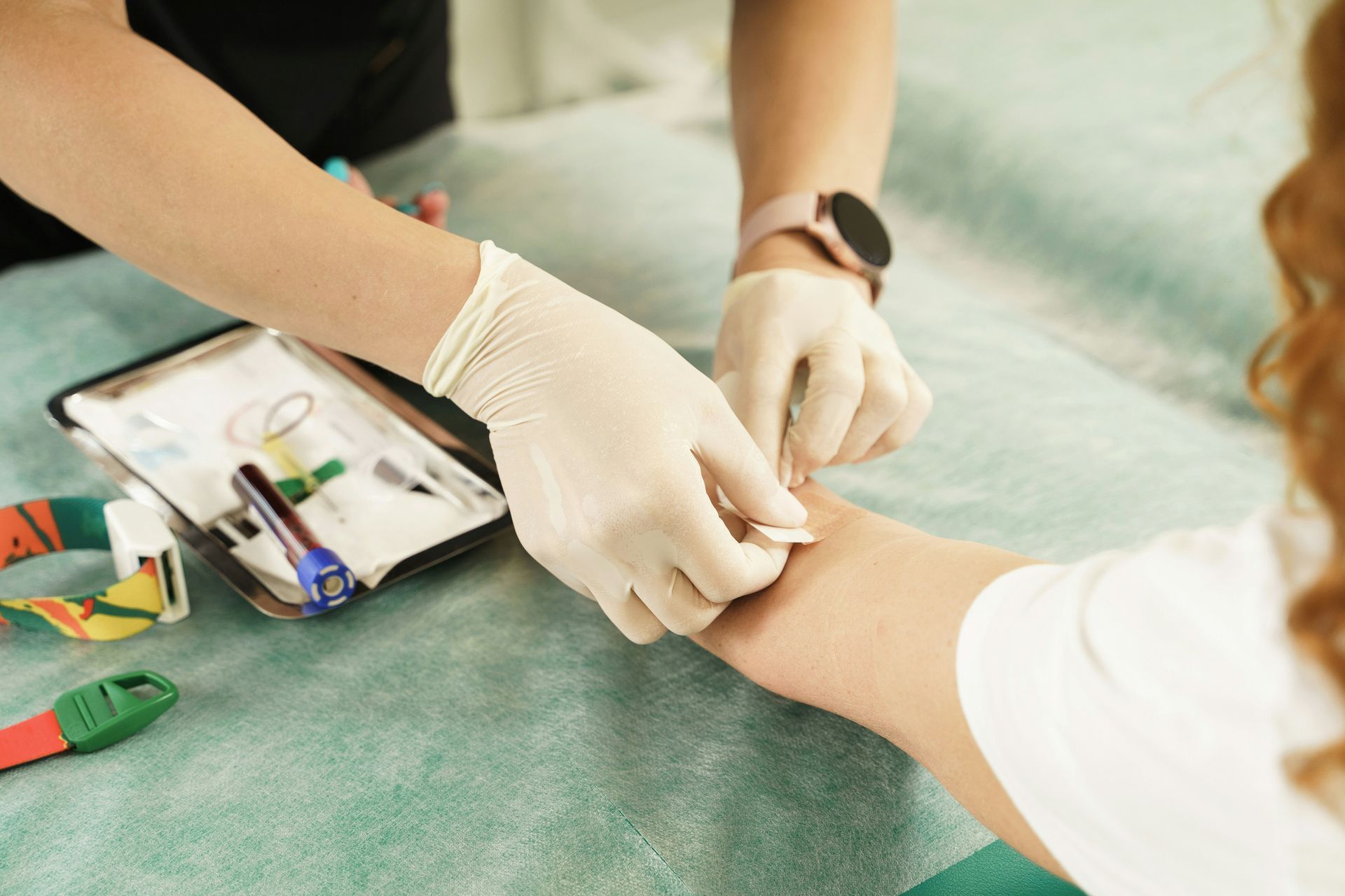 Gloved healthcare worker bandaging a patient’s arm on a clinic table with medical supplies nearby