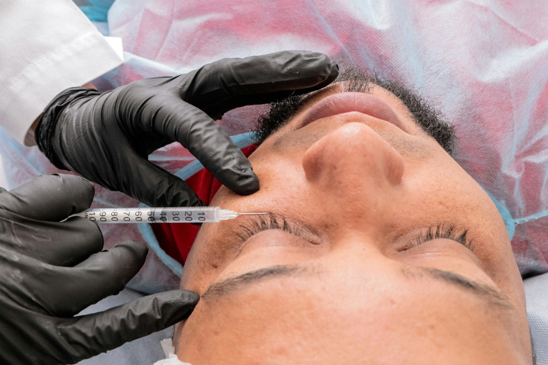 Gloved hands inject filler into a patient’s forehead during a cosmetic procedure