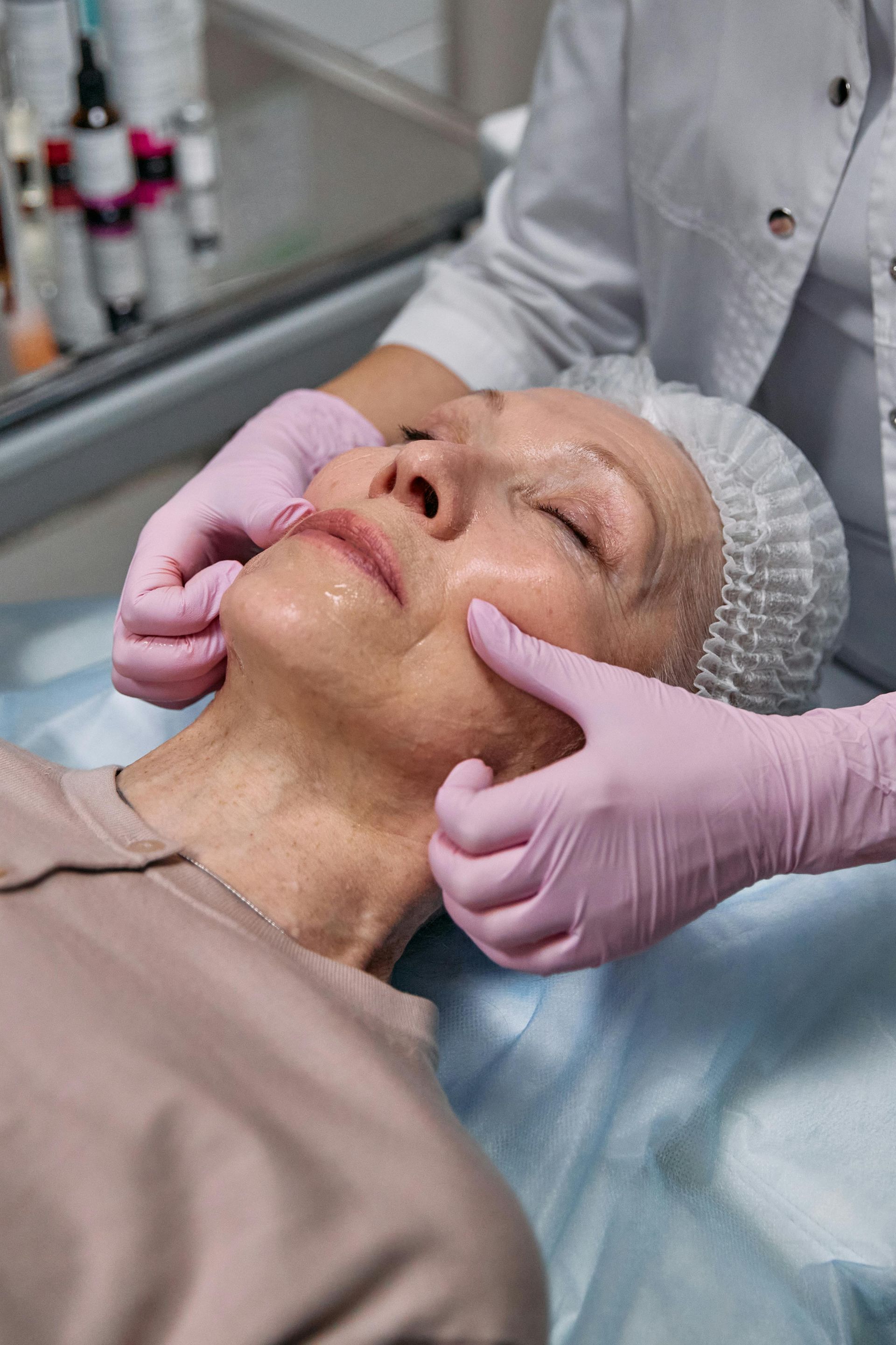 Gloved hands performing a facial massage on a reclining client in a spa or clinic setting