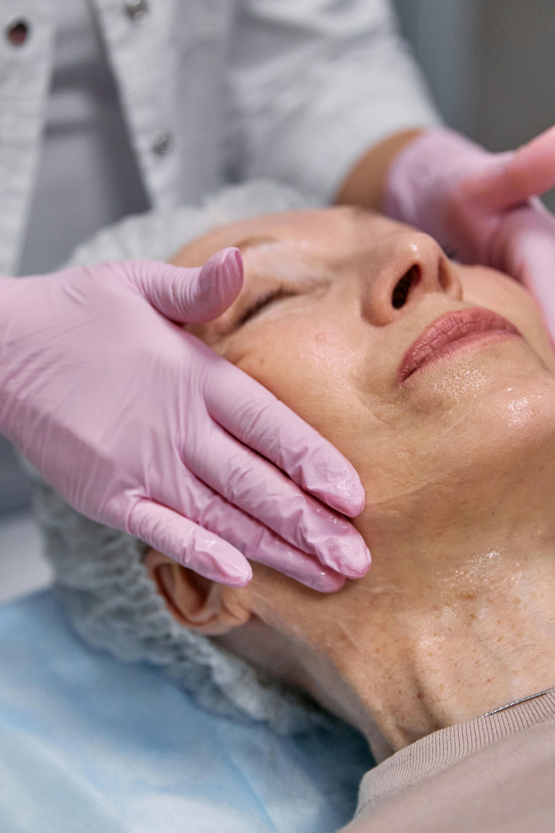 Gloved hands massage a woman's face during a spa facial treatment