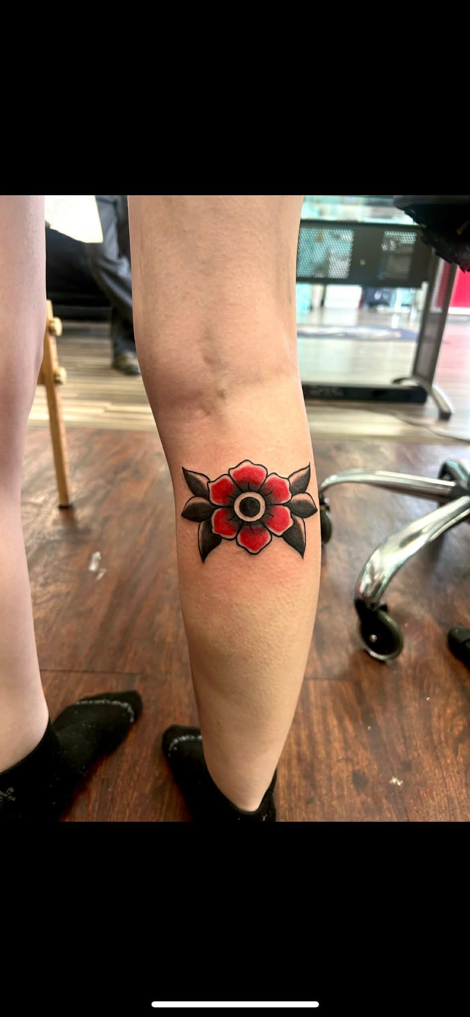 A red flower tattoo with black accents on a person's leg.