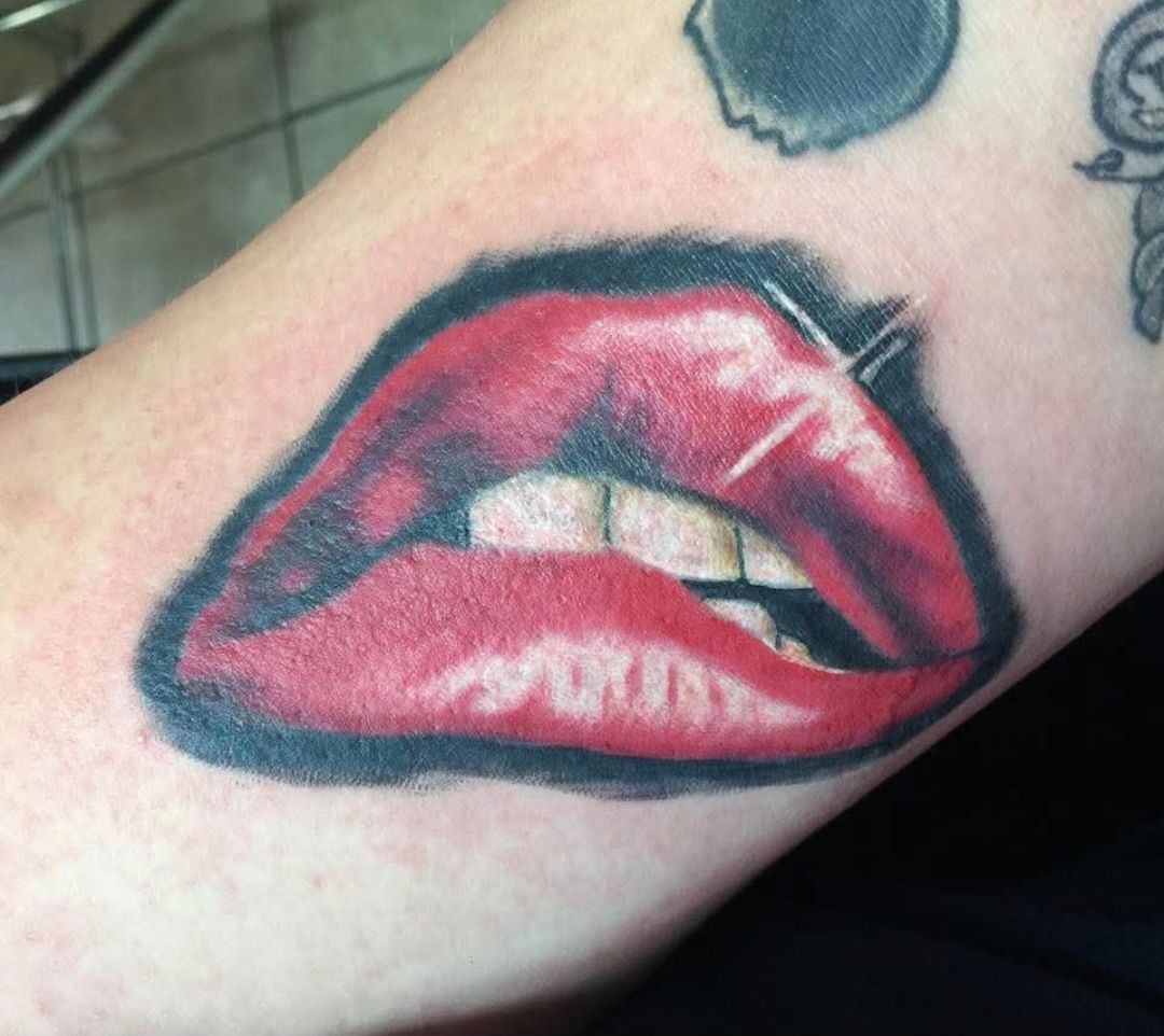 Tattoo of red lips with a black outline on an arm. Teeth visible.
