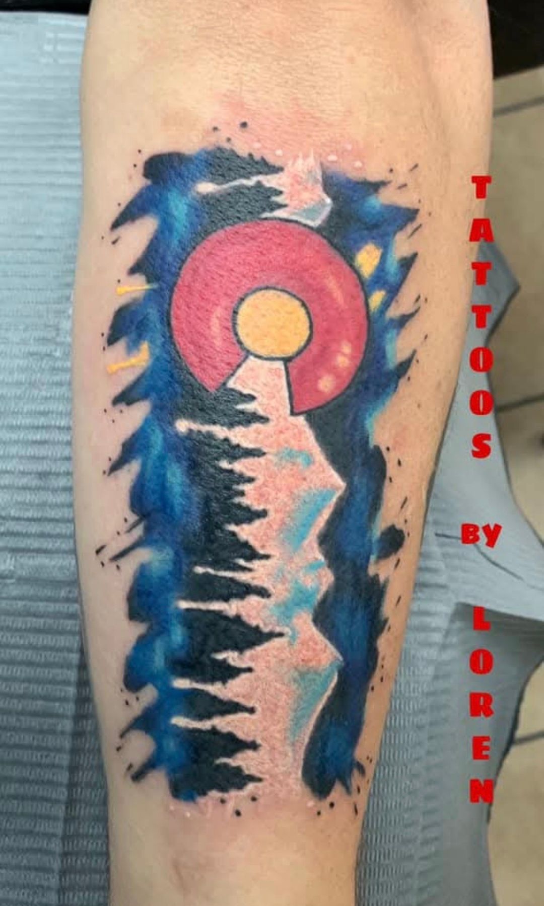 Tattoo on arm; Colorado state flag design with blue night sky, mountain, and pine trees.