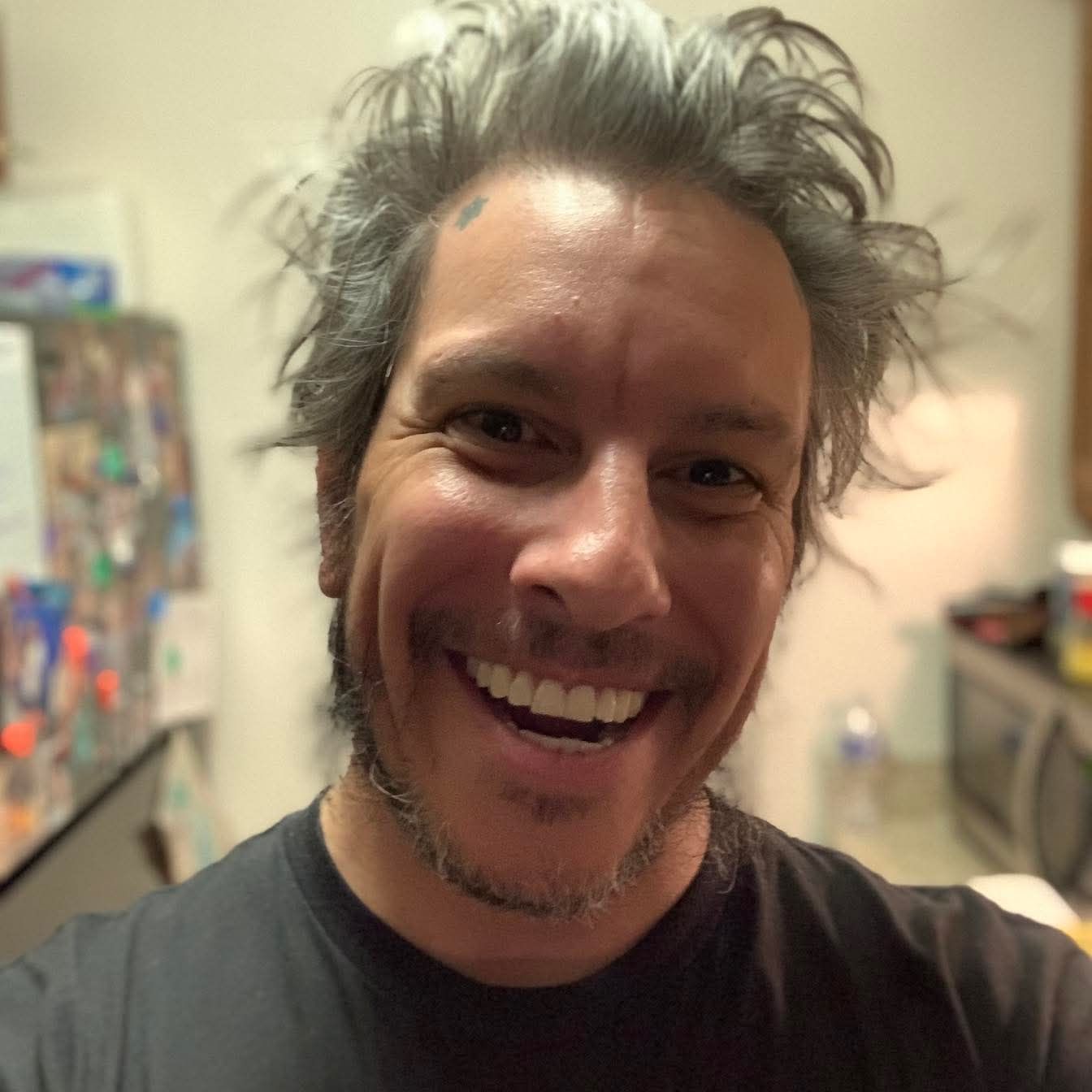 Man with gray, messy hair, smiling broadly in a kitchen setting.