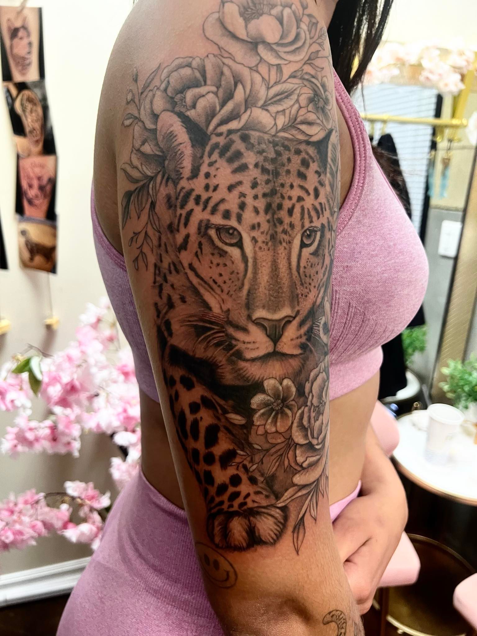 Tattoo of a leopard with flowers on a person's upper arm, in a room with pink and gold décor.