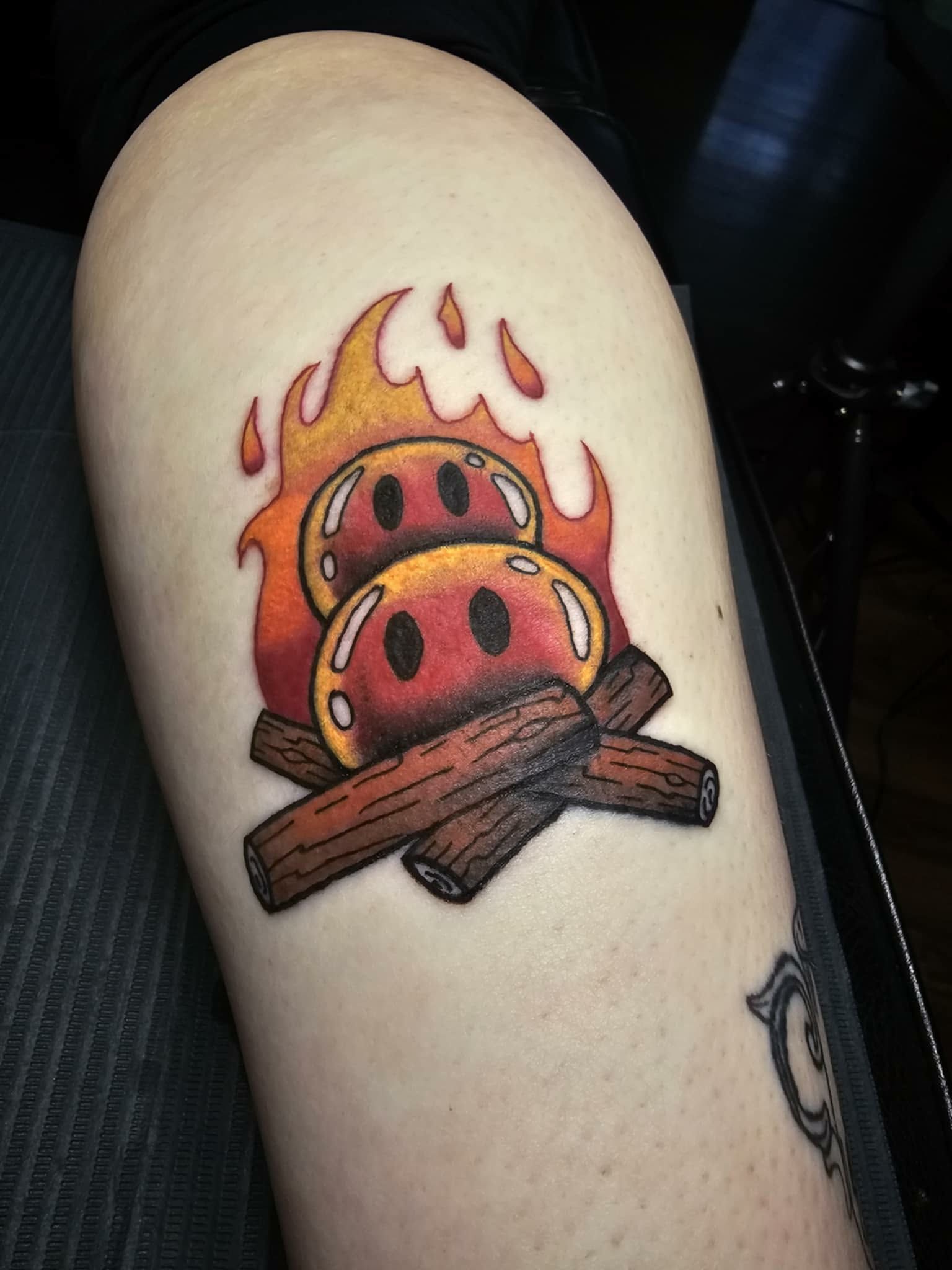 Tattoo of two smiling, burning mushrooms on logs with flames.