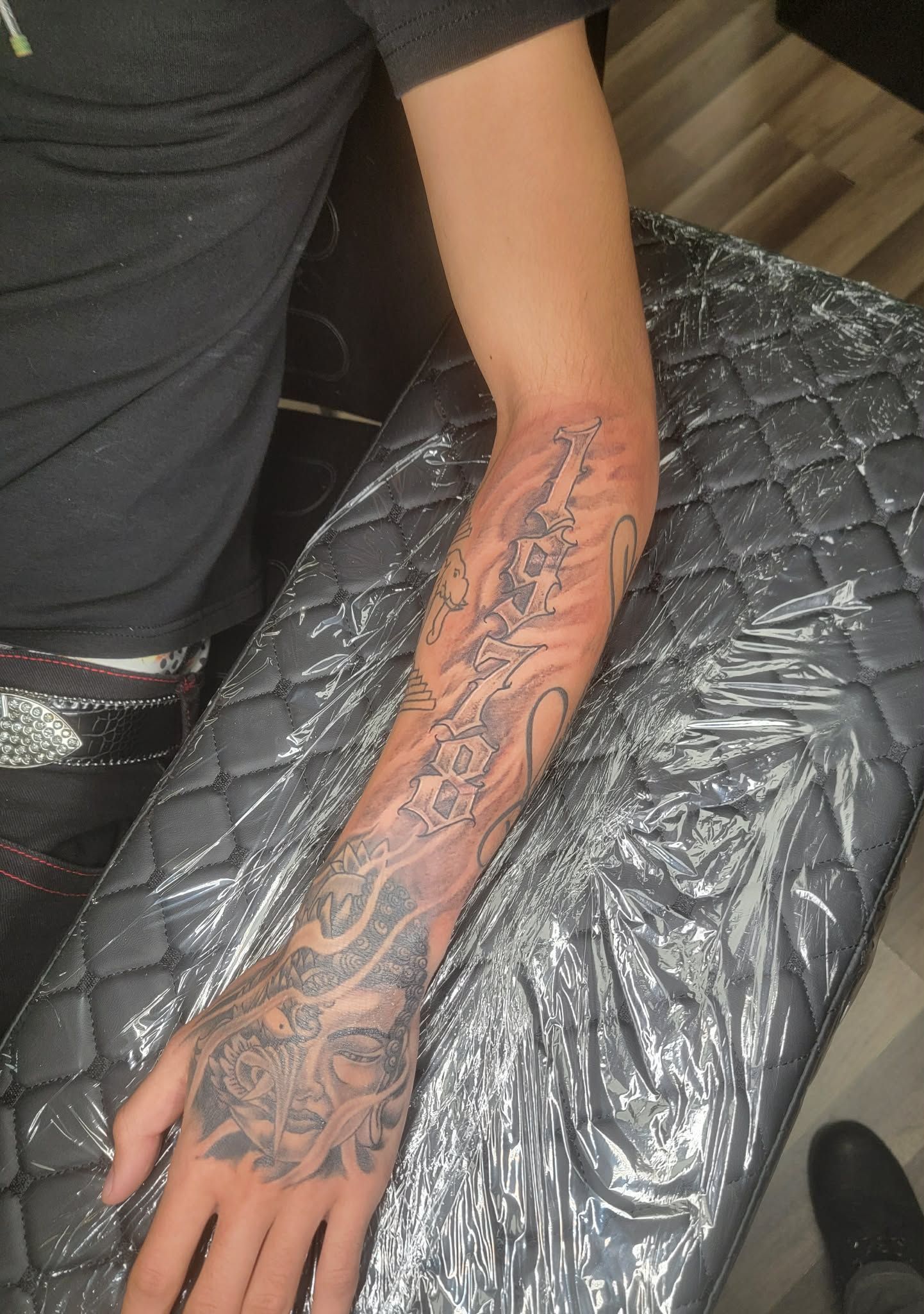 Arm with detailed tattoo from wrist to elbow; sitting on a tattoo table.