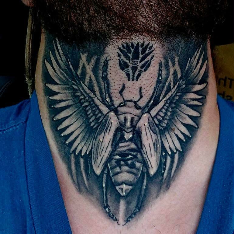 Tattoo of a beetle with wings on a person's neck; grayscale.