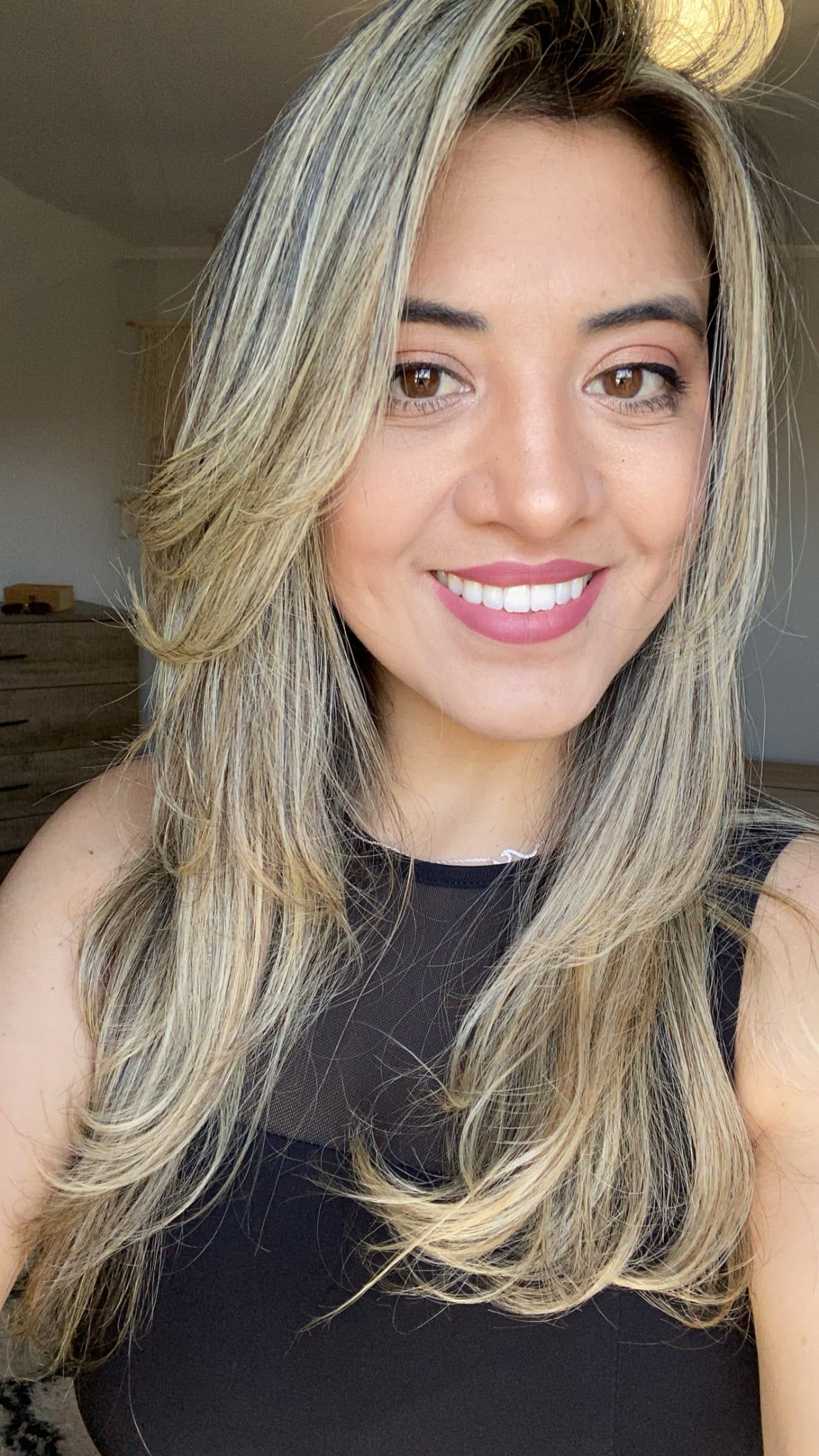 Woman with long blonde hair smiles, wearing a black top.