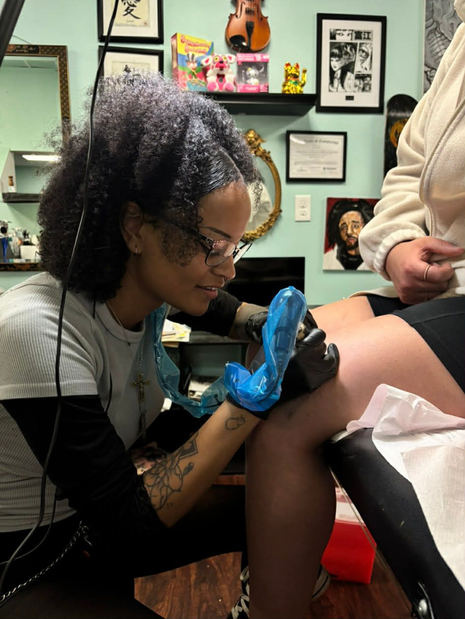 Tattoo artist with black gloves tattoos a person's leg in a studio.