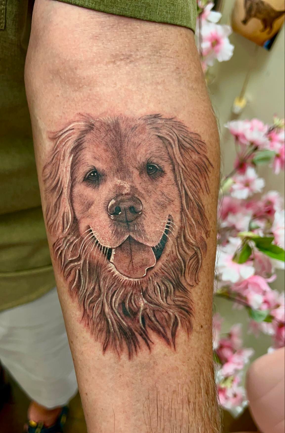 Golden retriever dog portrait tattoo on arm, smiling, brown and tan, with floral background.