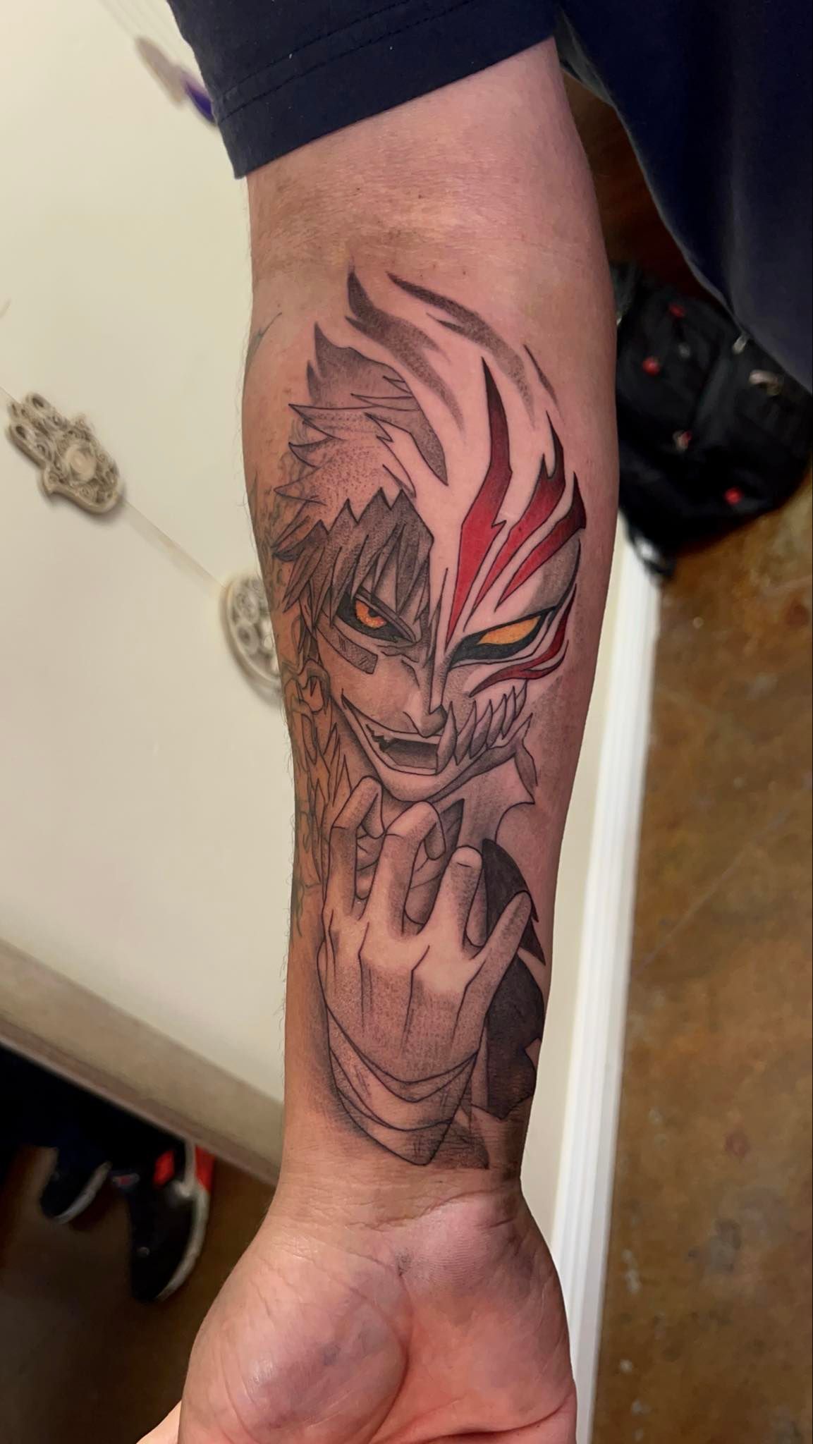 Tattoo of Ichigo Kurosaki from Bleach on an arm; detailed black and red ink, character's face split.