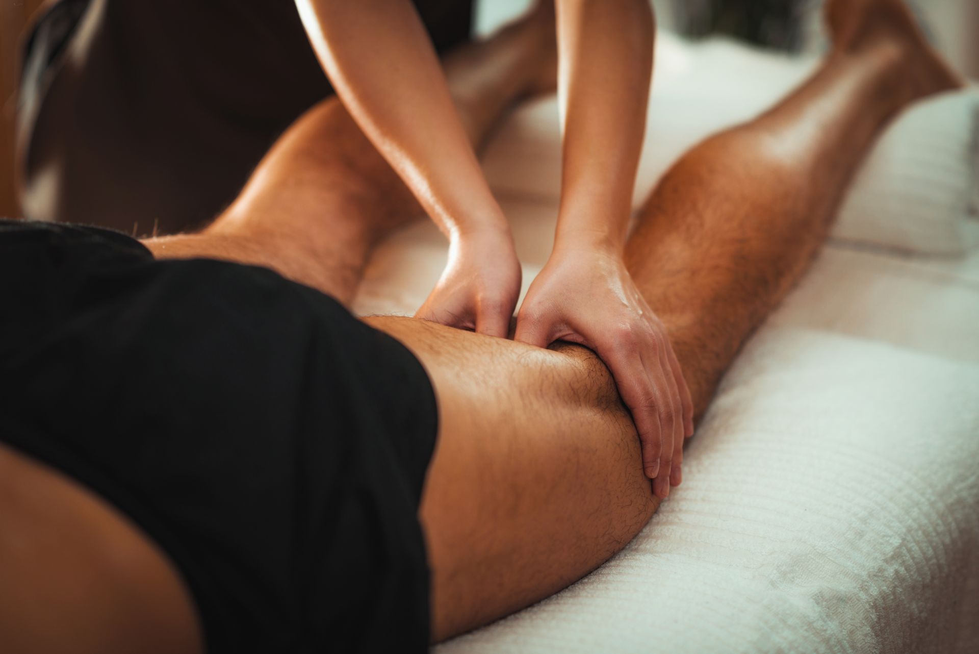 A physical therapist in a blue shirt performs a leg stretch on a patient lying on a treatment table in a gym. A physical therapist in a blue shirt performs a leg stretch on a patient lying on a treatment table in a gym.