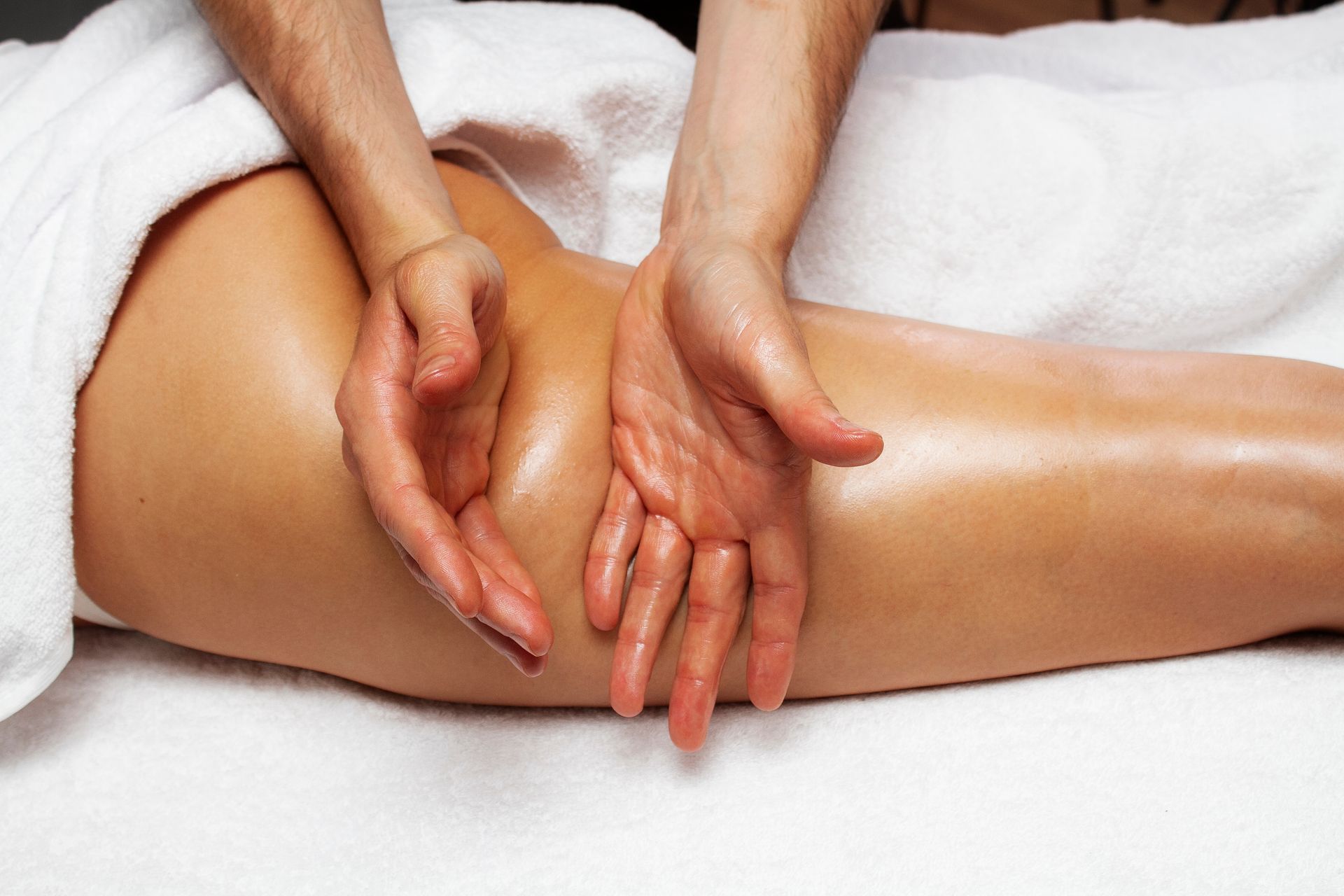 A person receives a professional facial massage while lying down on a white surface with their eyes closed.