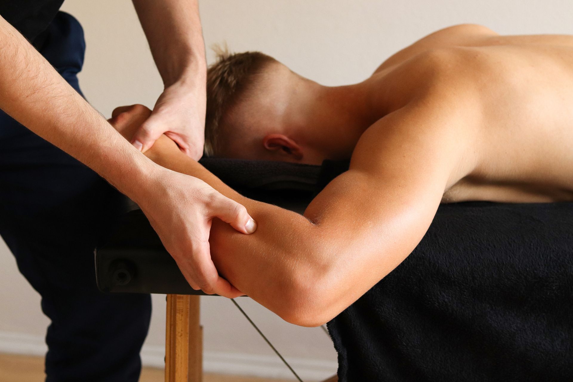 A physical therapist in a blue shirt performs a leg stretch on a patient lying on a therapy table in a blue room. A physical therapist in a blue shirt performs a leg stretch on a patient lying on a therapy table in a blue room.