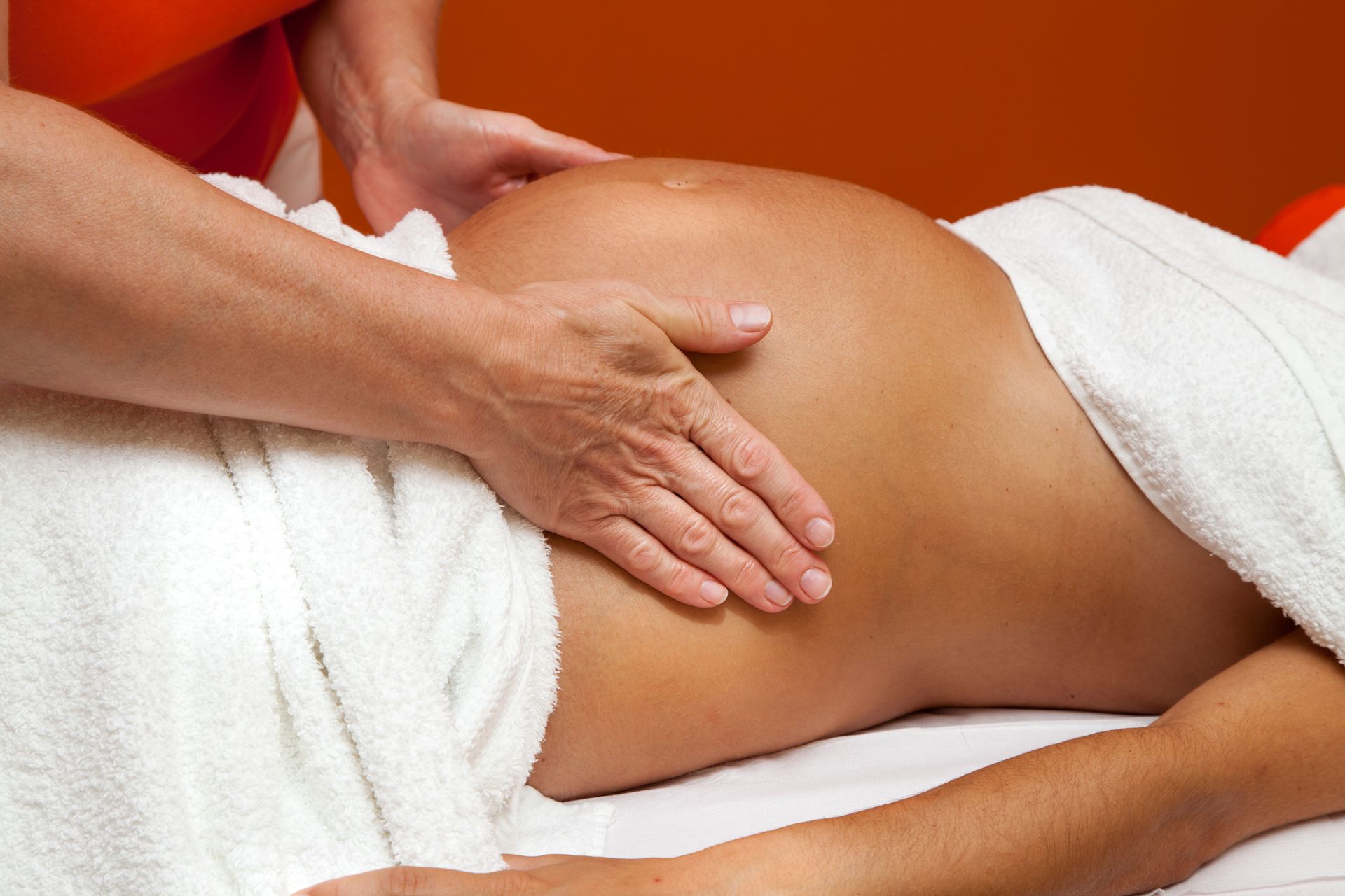 Hands gently massaging the abdomen of a pregnant person resting on a table draped with a white towel.