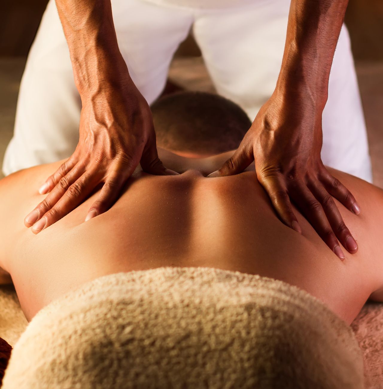 A person receiving a back massage with hands pressing into their upper shoulders.