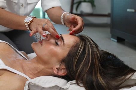 A practitioner performs a facial massage on a person lying down, applying gentle pressure between their eyes and forehead.