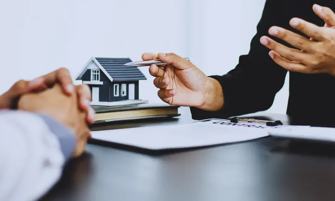 A person is holding a pen in front of a model house.