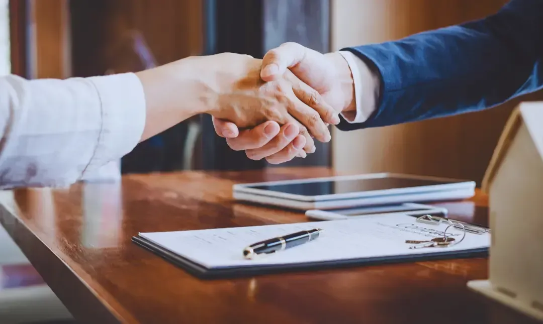 A man and a woman are shaking hands over a table.