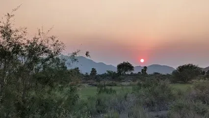 A sunset over a field with trees and mountains in the background.