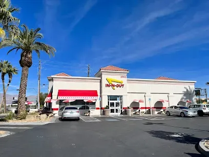 A white and red in n out burger restaurant with cars parked in front of it.