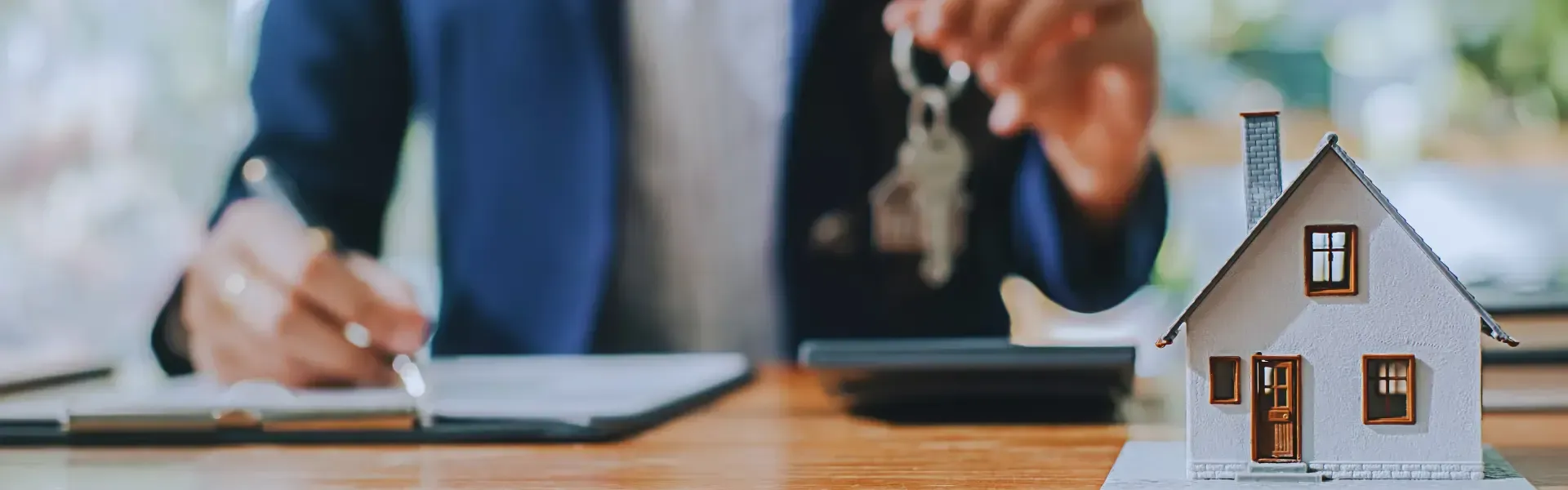 A man is holding a pair of keys next to a model house.