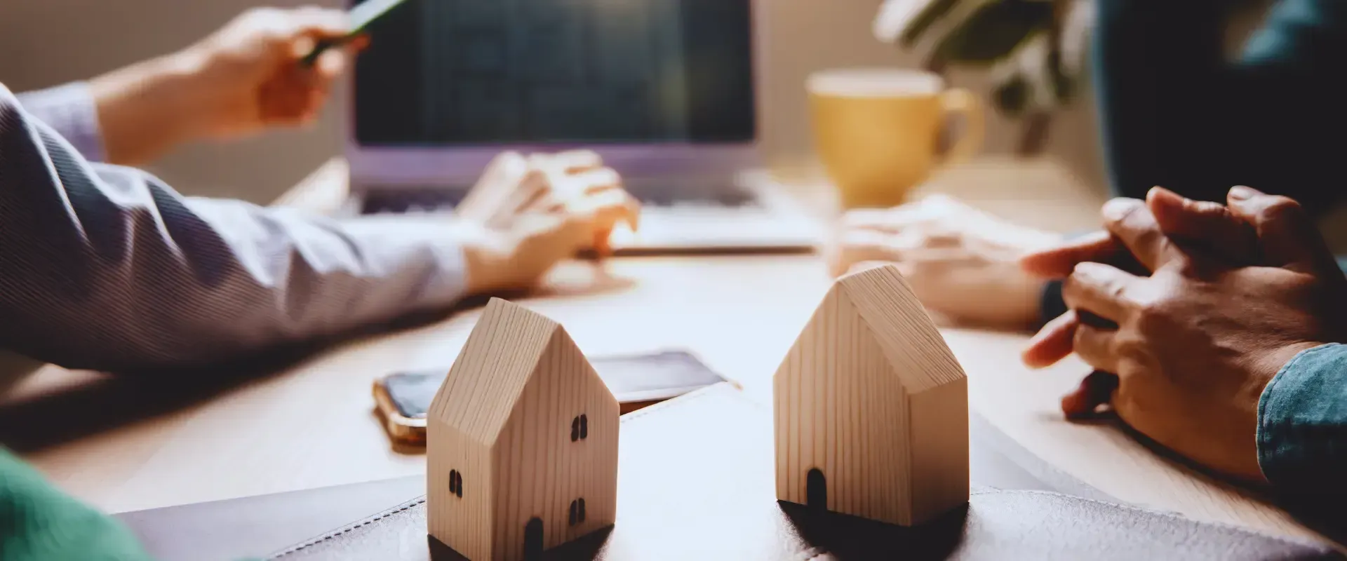 A group of people are sitting at a table with wooden houses and a laptop.