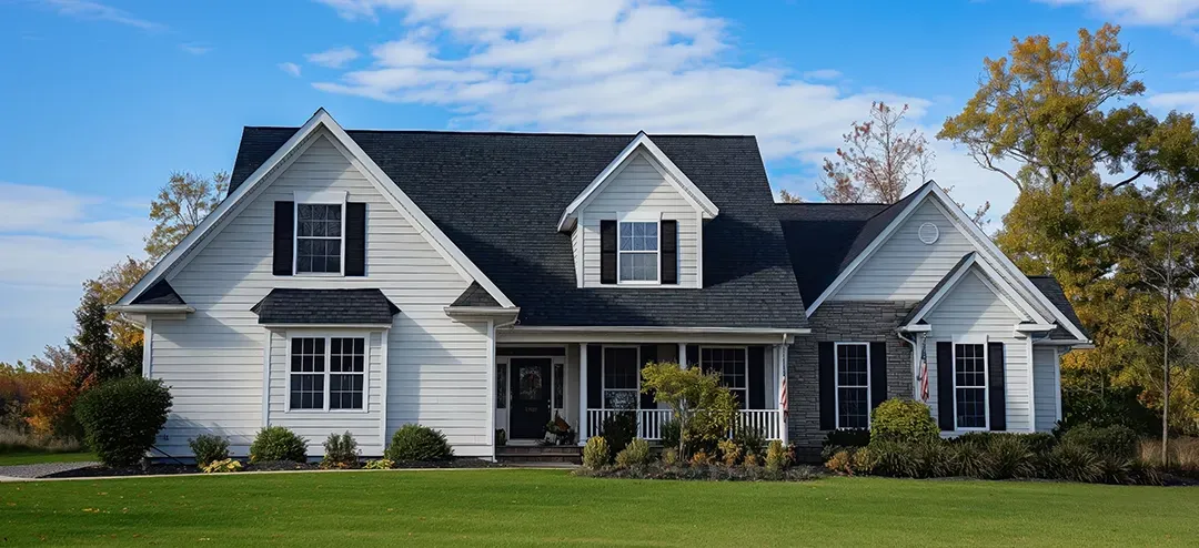 A large white house with a black roof is sitting on top of a lush green lawn.