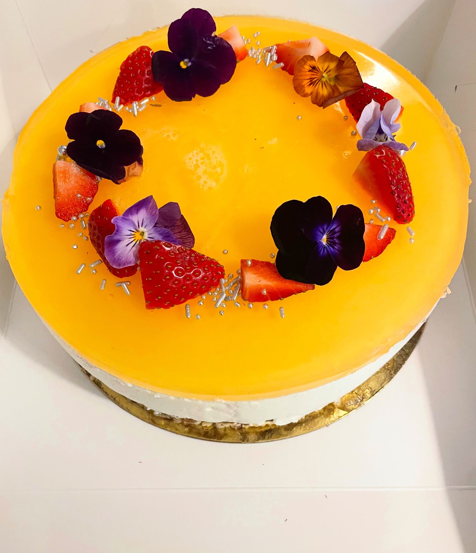 Gul glaseret kage toppet med jordbær og lilla spiselige blomster på en hvid tallerken