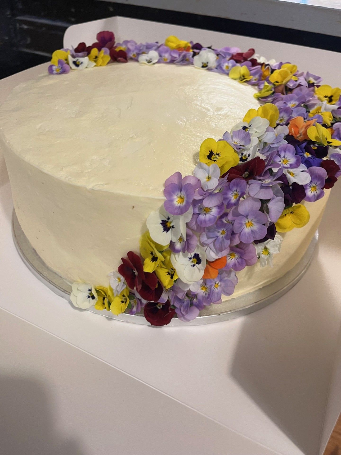 Kage med smørcremeglasur dekoreret med farverige spiselige blomster.