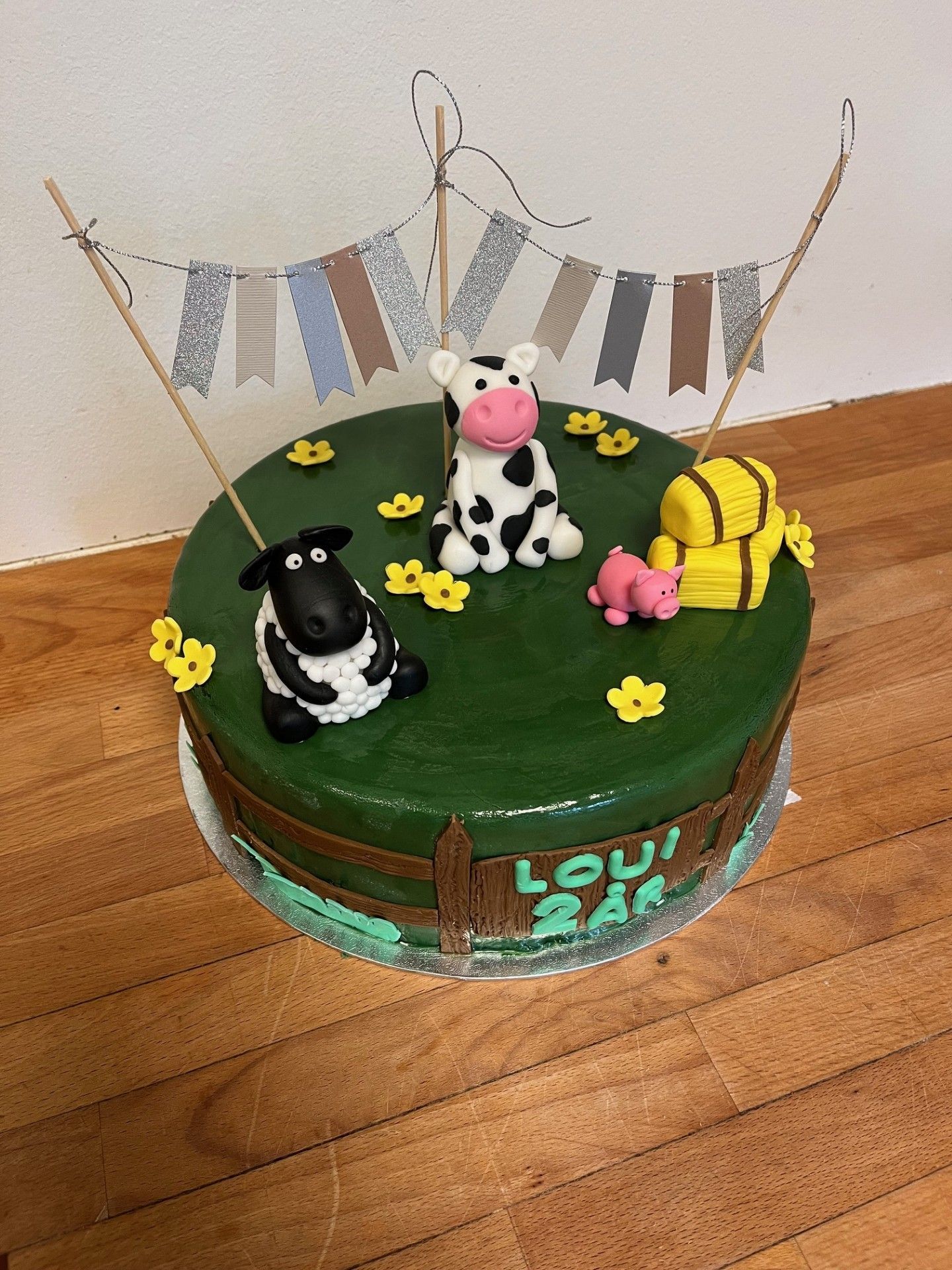 Kage med gårdtema med ko, får, gris, høballer og banner på grøn frosting, træbordbaggrund.