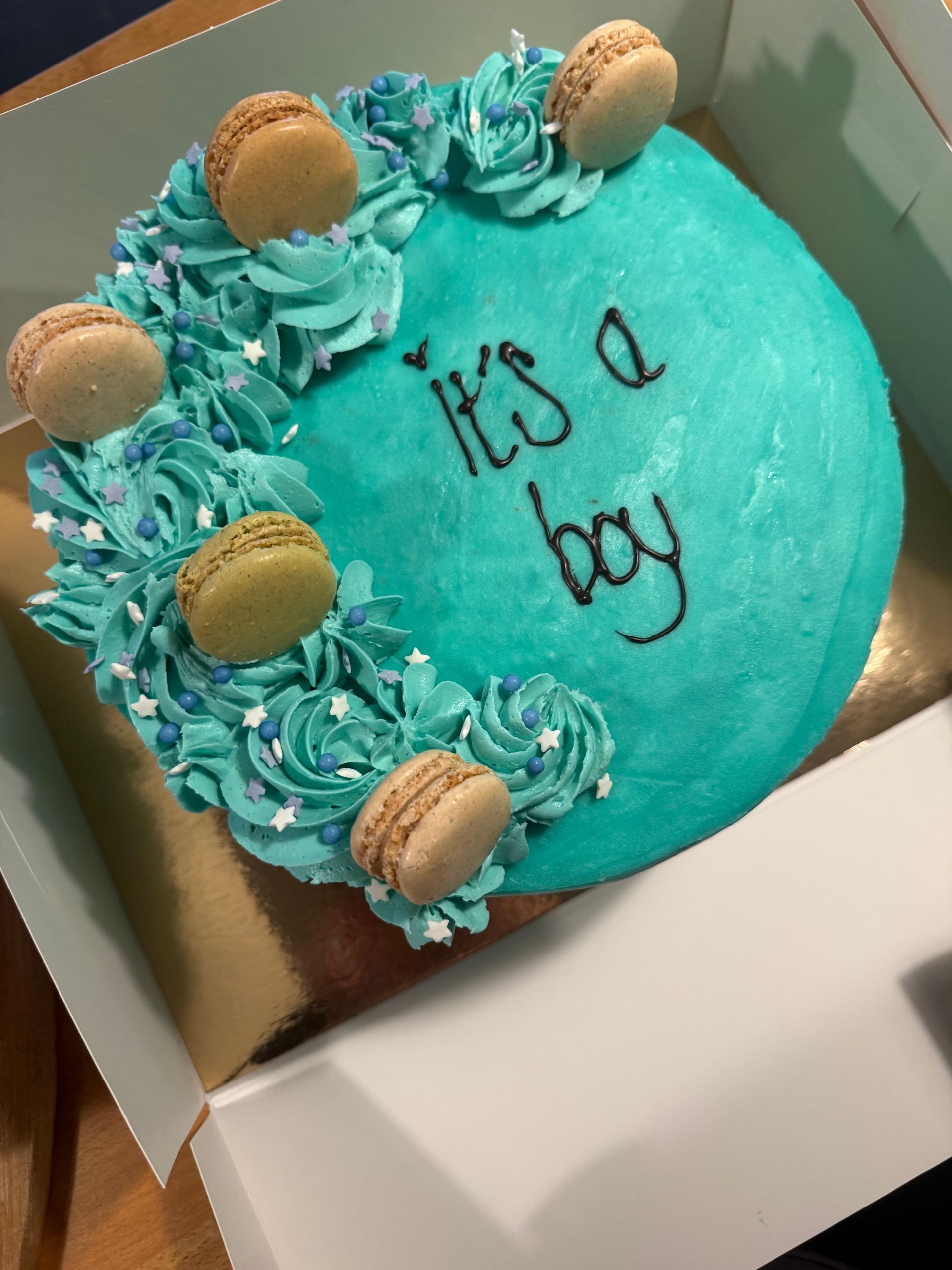 Turkis frostet kage i en æske, dekoreret med blå hvirvler og macarons, med teksten