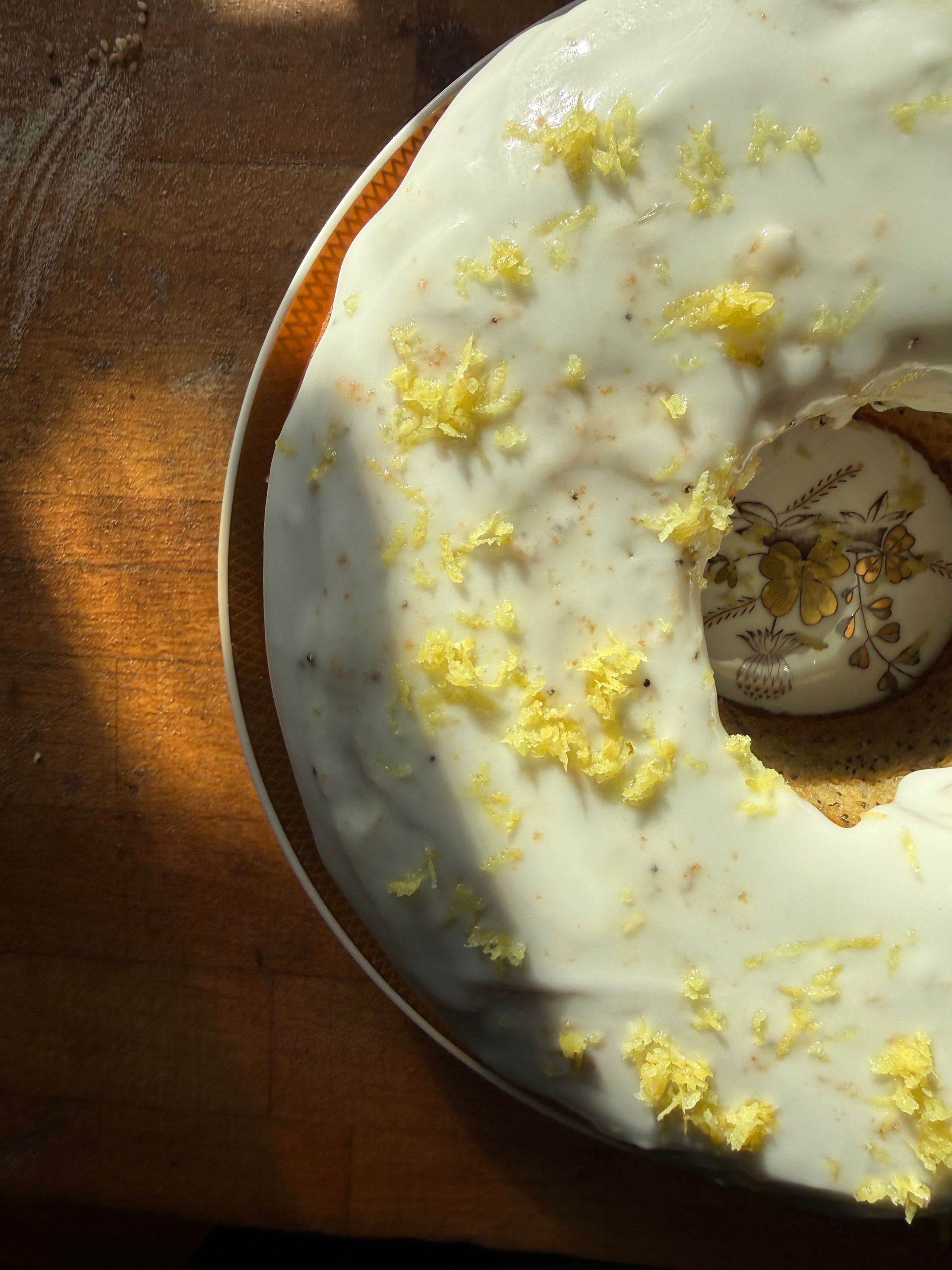 Hvid glaseret bundtkage med gul skal på en tallerken, oplyst af varmt sollys.