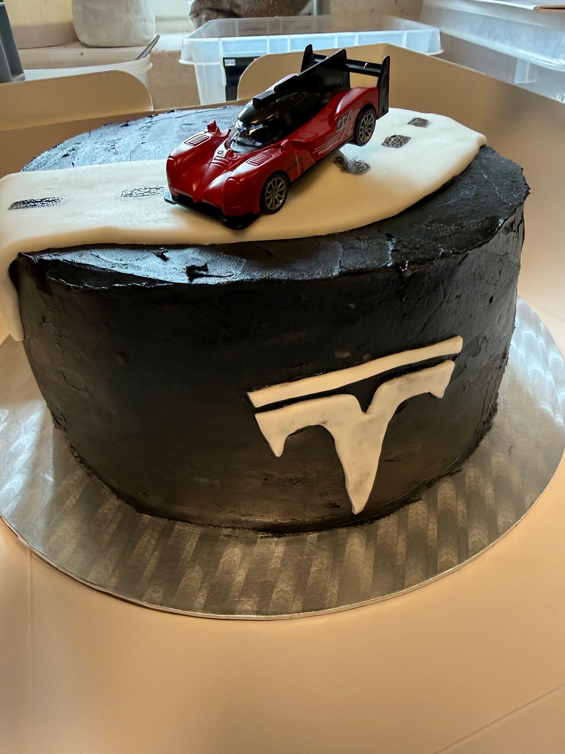 Sort Tesla-tema kage med en rød biltopping på et sølvbræt