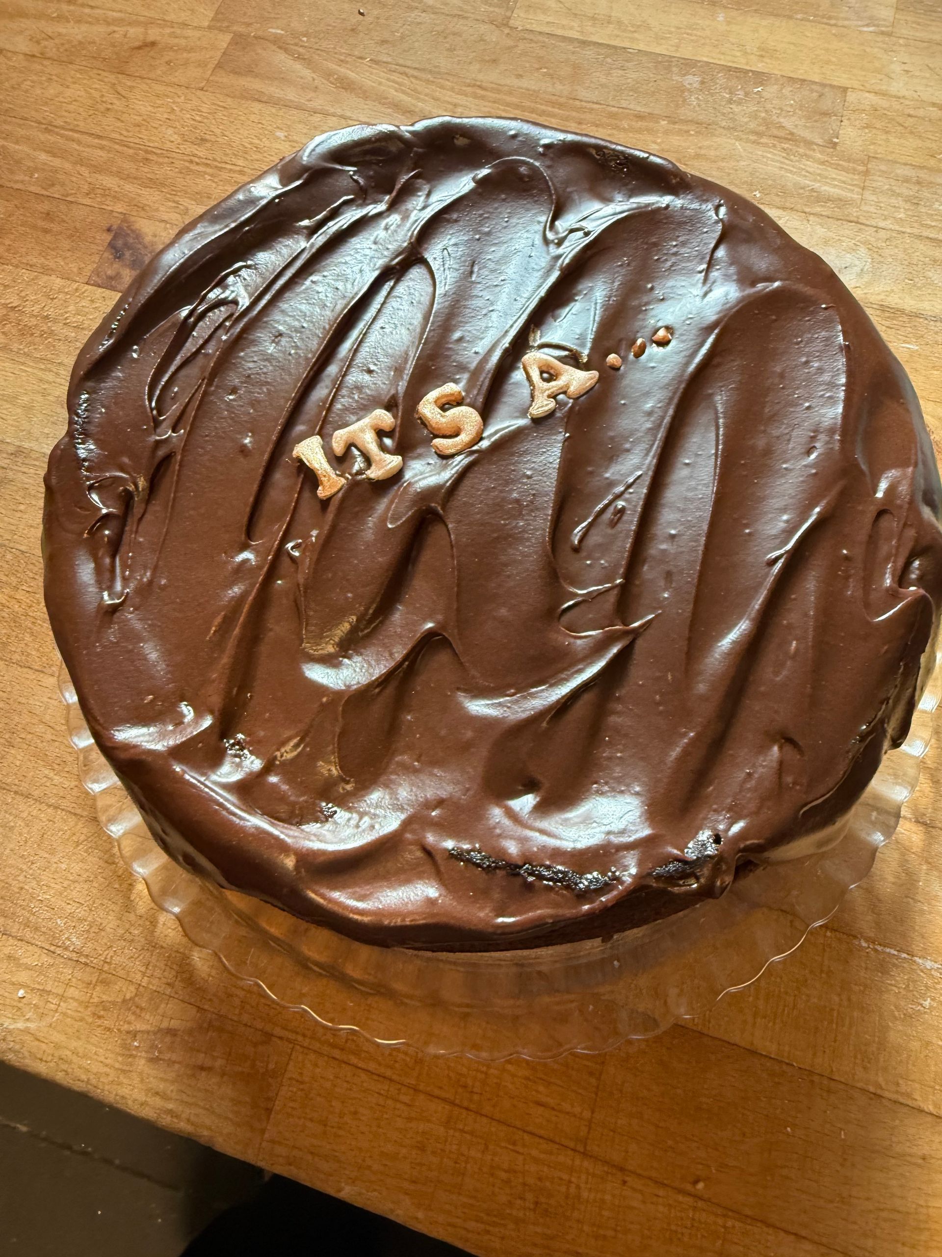 Rund chokoladeglasureret kage med guldskrift på et træbord