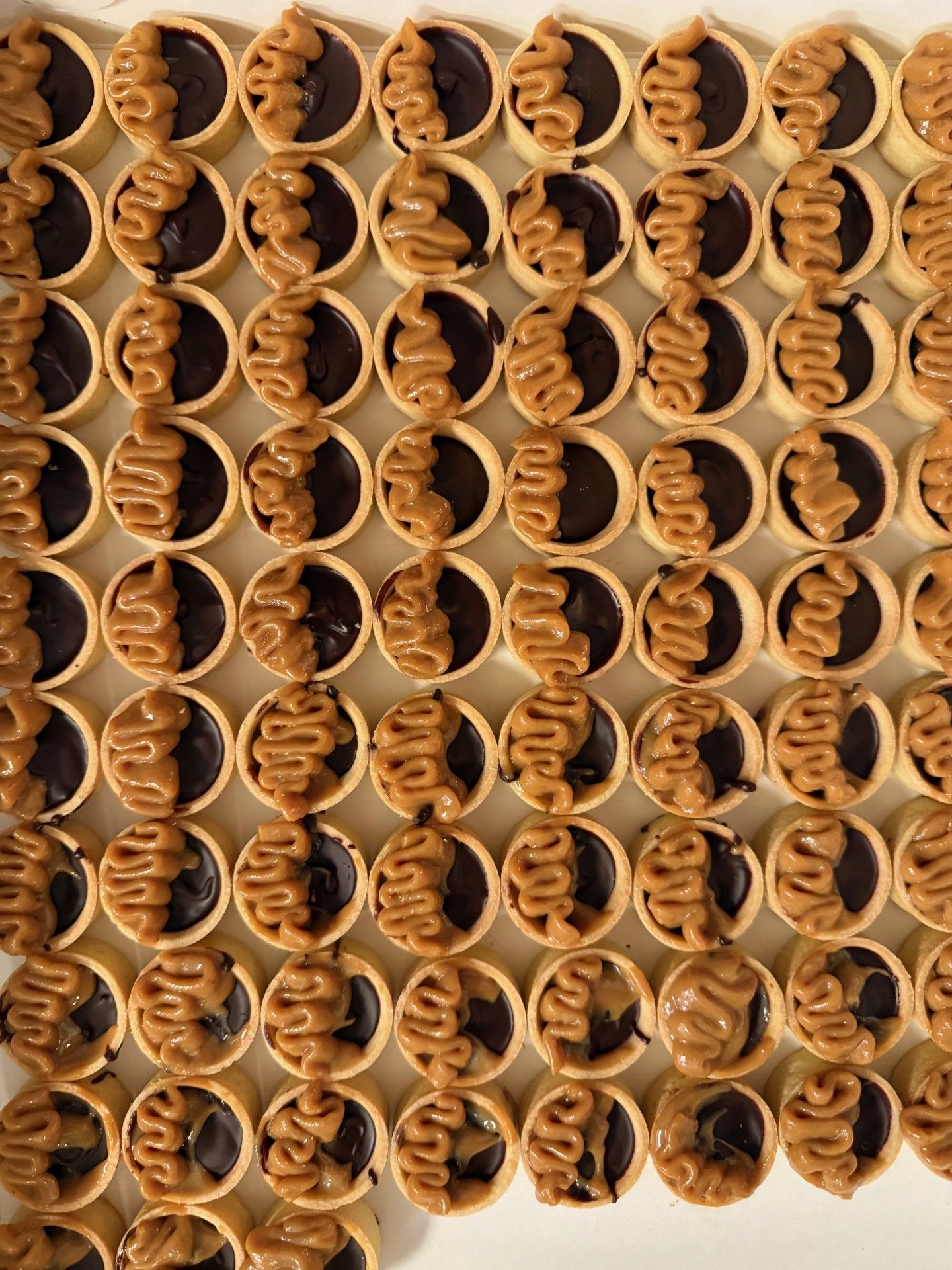 Rækker af mini chokoladetærter med karameldrys på en lys overflade.