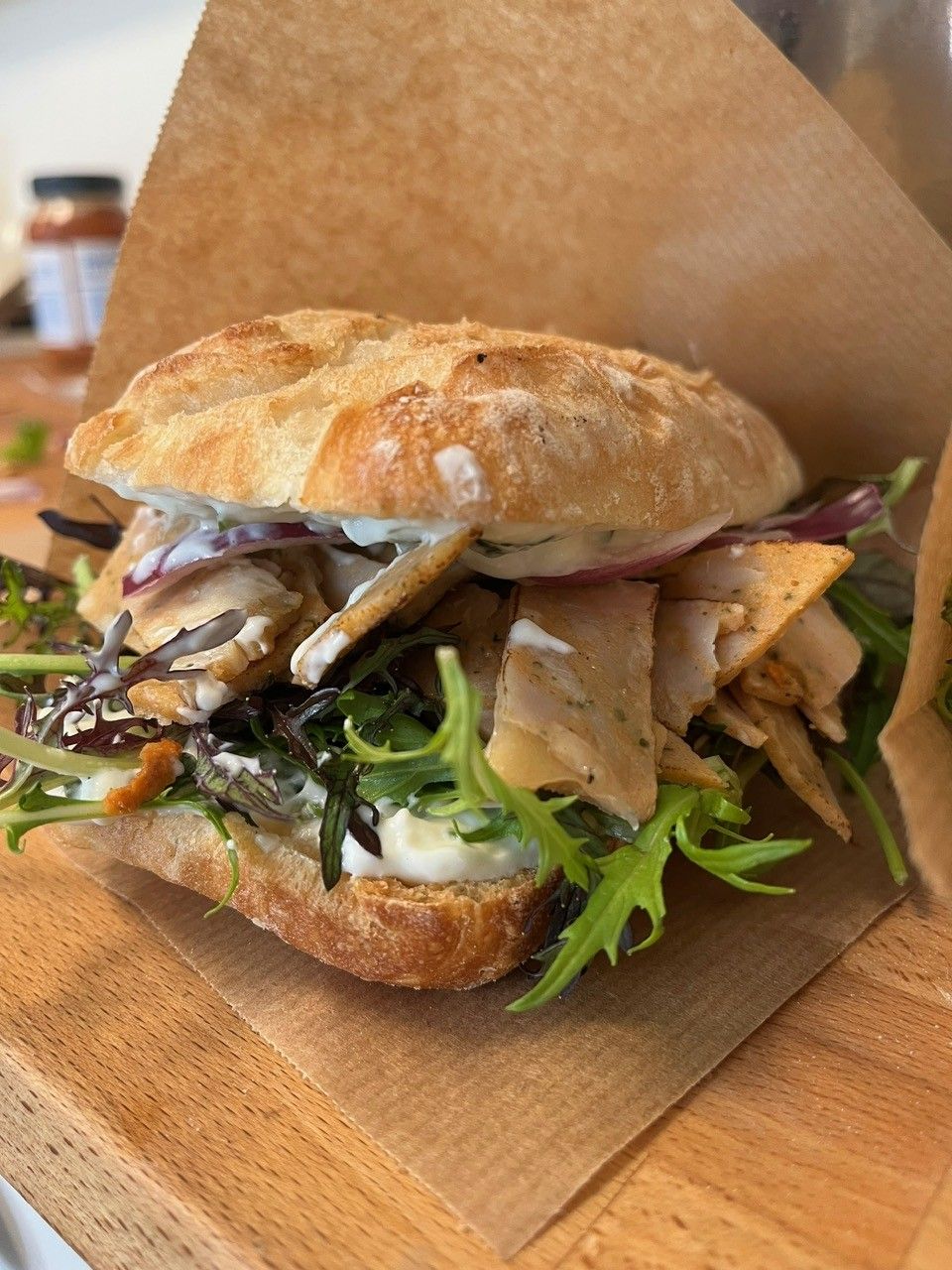 Sandwich på en træoverflade med røget fisk, grøntsager og rødløg på en ciabatta-bolle.
