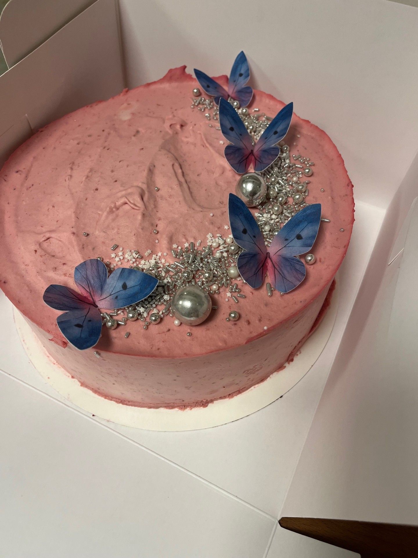 Lyserød frostet kage dekoreret med blå sommerfugletopper og sølvkrymmel.