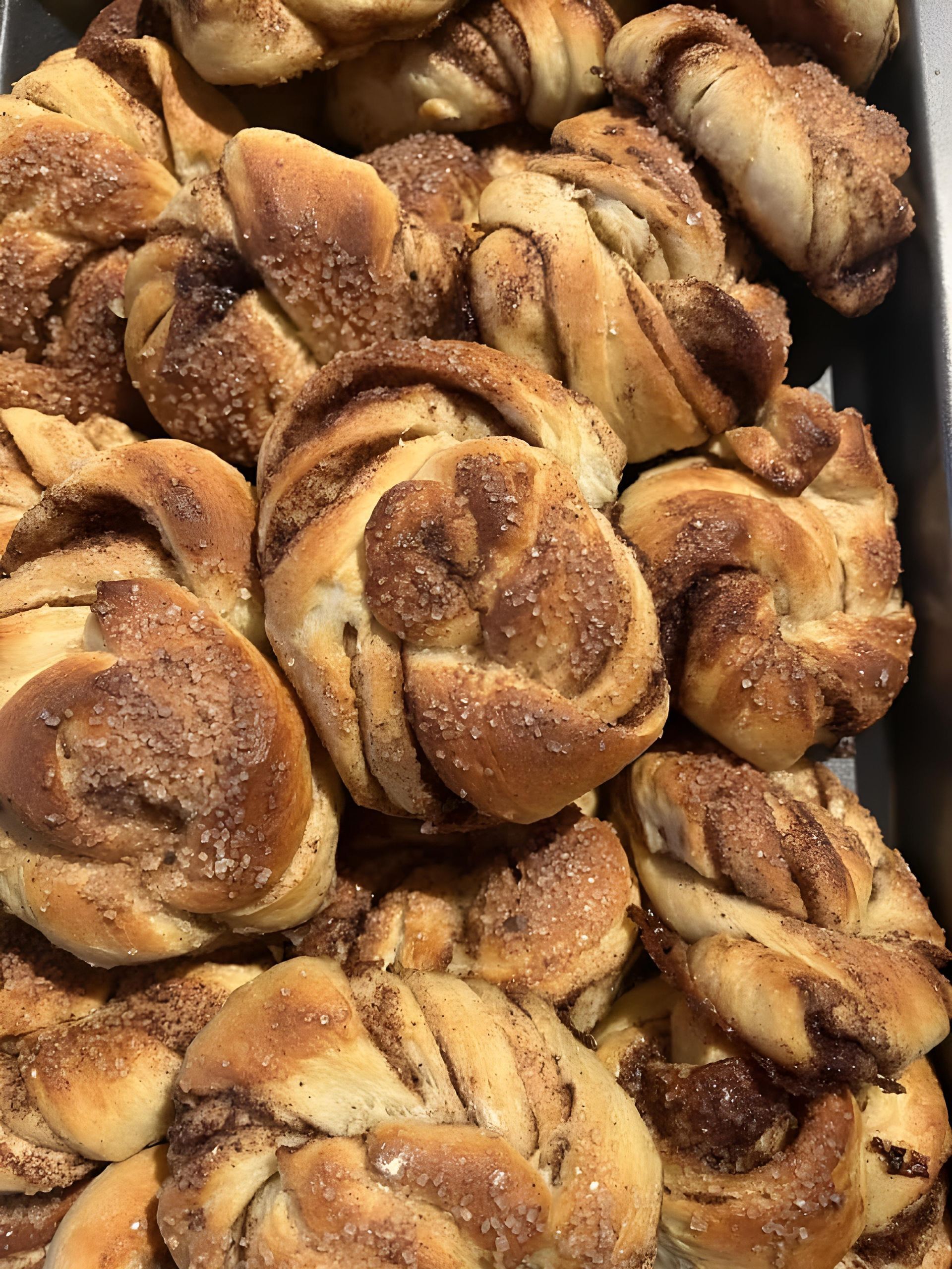 Bakke med gyldenbrune kanelsnegler drysset med sukker, tæt pakket sammen