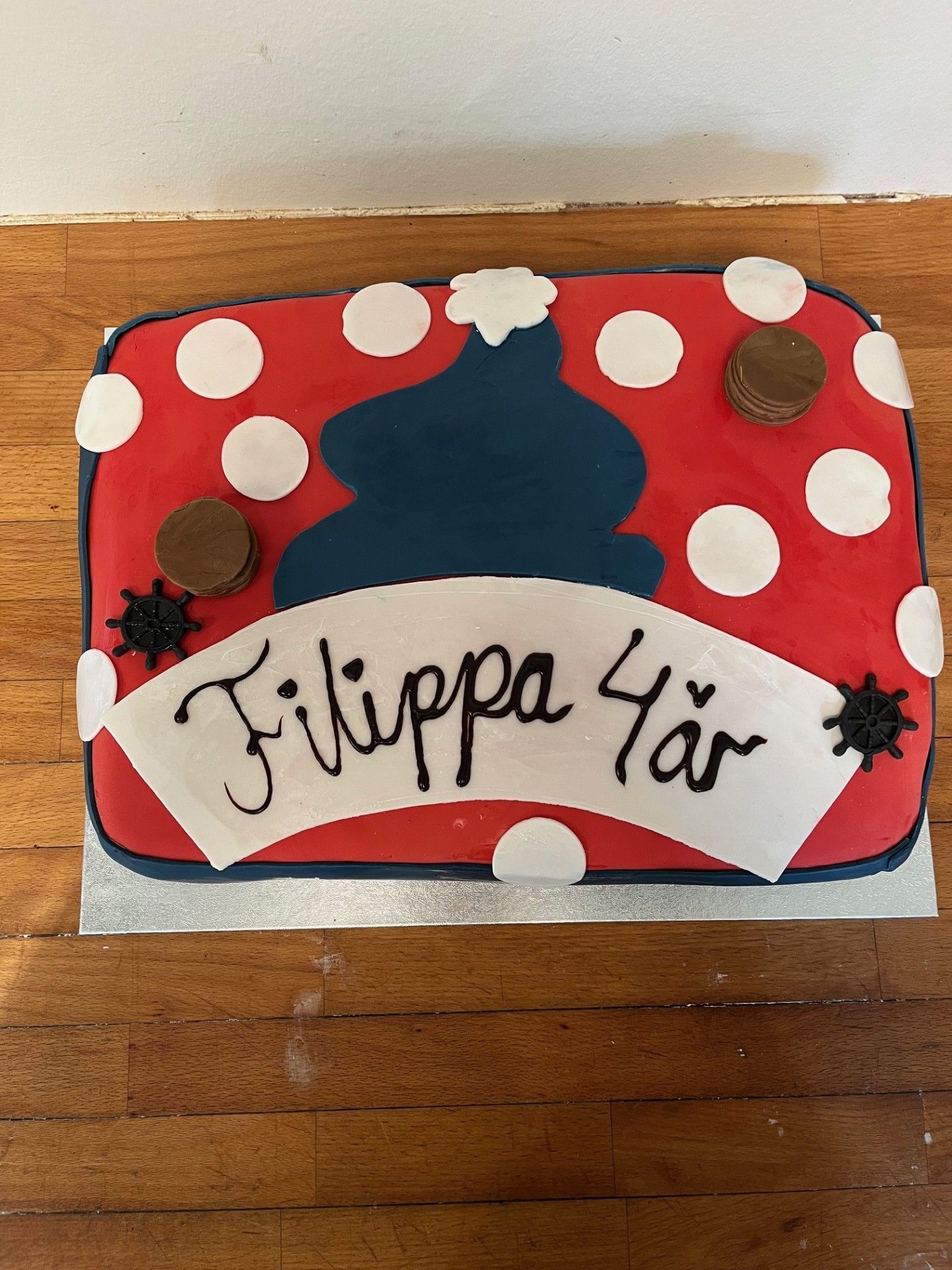 Fødselsdagskage dekoreret i rødt med hvide polkaprikker, blå frosting og et banner med teksten